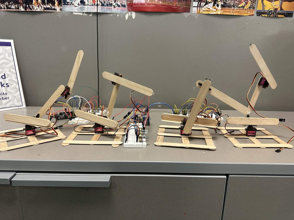 Row of student-built robotic arm projects made from popsicle sticks and servos