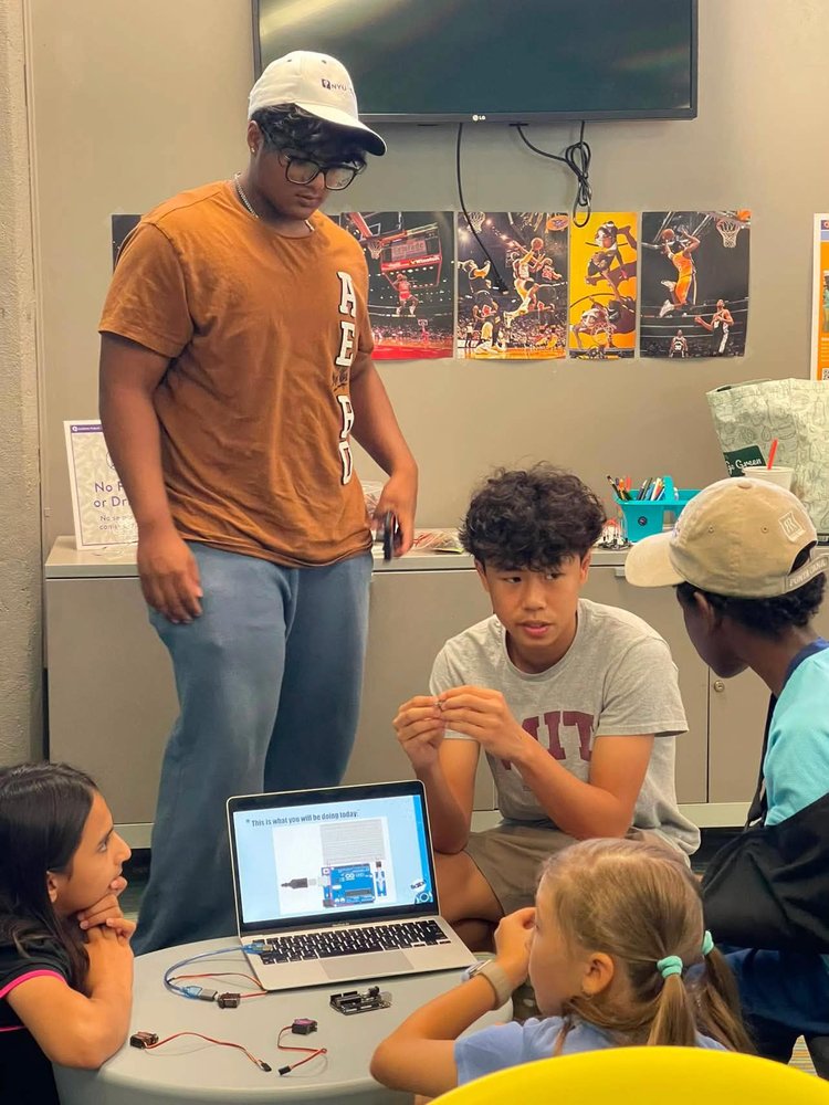 Mentor and students gathered around a laptop and circuit components during a workshop