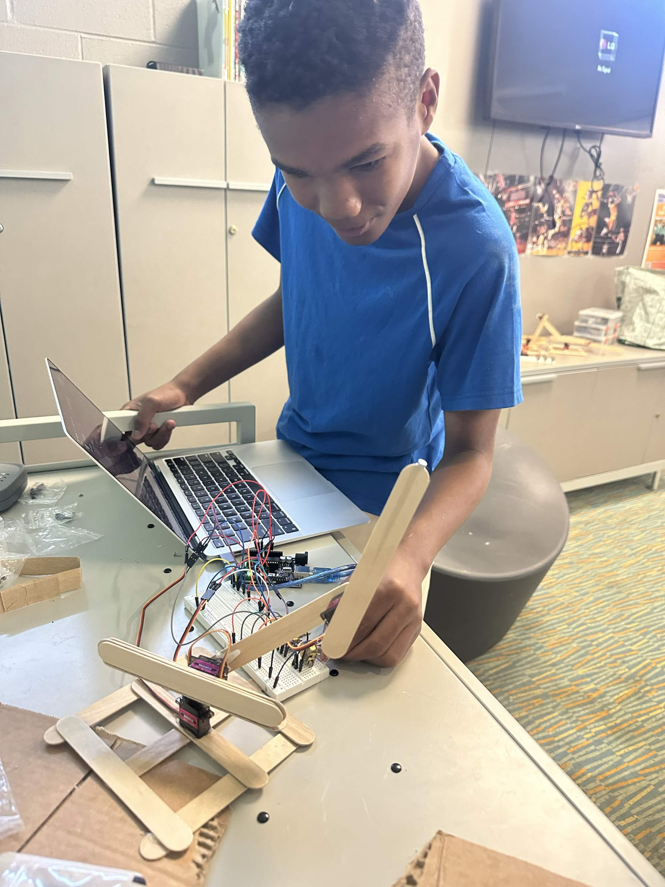 Student building a robotic arm project with a laptop and breadboard